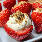 A close-up of hollowed strawberries filled with cream and topped with crumbled cookies and chocolate chips.