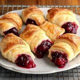 A plate of flaky, golden-brown pastries filled with a dark cherry filling, some oozing slightly from the sides.