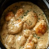 A creamy chicken and biscuit dish garnished with parsley, served in a black slow cooker.