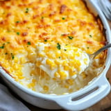 A spoonful of creamy corn casserole is lifted from a baked dish topped with a golden cheese crust.