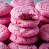 A stack of pink cookies, one with a bite taken out of it, is surrounded by more cookies.