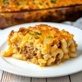 A serving of cheesy baked macaroni and cheese with ground beef, garnished with parsley, on a white plate.