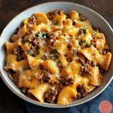 A bowl of pasta with ground beef and melted cheese, garnished with fresh parsley.