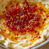 A close-up of a creamy dish topped with a glossy red sauce and mustard seeds.