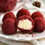 A plate of red velvet cake balls, some whole and one cut in half, revealing a creamy white filling inside.