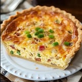 A sliced quiche with a golden crust, filled with eggs, vegetables, and garnished with chopped green onions.