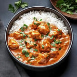 A bowl of creamy chicken curry garnished with fresh herbs served over fluffy white rice.