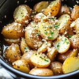 A close-up of seasoned and buttered halved baby potatoes sprinkled with herbs and breadcrumbs in a dark bowl.