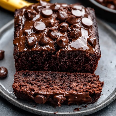 A rich chocolate loaf cake is displayed with a slice cut and topped with melted chocolate and chocolate chips.