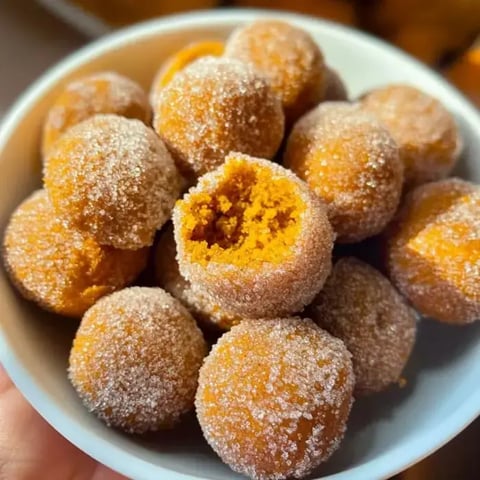 A bowl filled with round, sugar-coated orange snacks, one of which has a bite taken out of it.